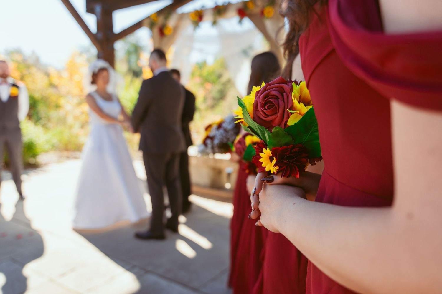 Close-up of red and orange floral bouquet with ceremony in soft focus background.