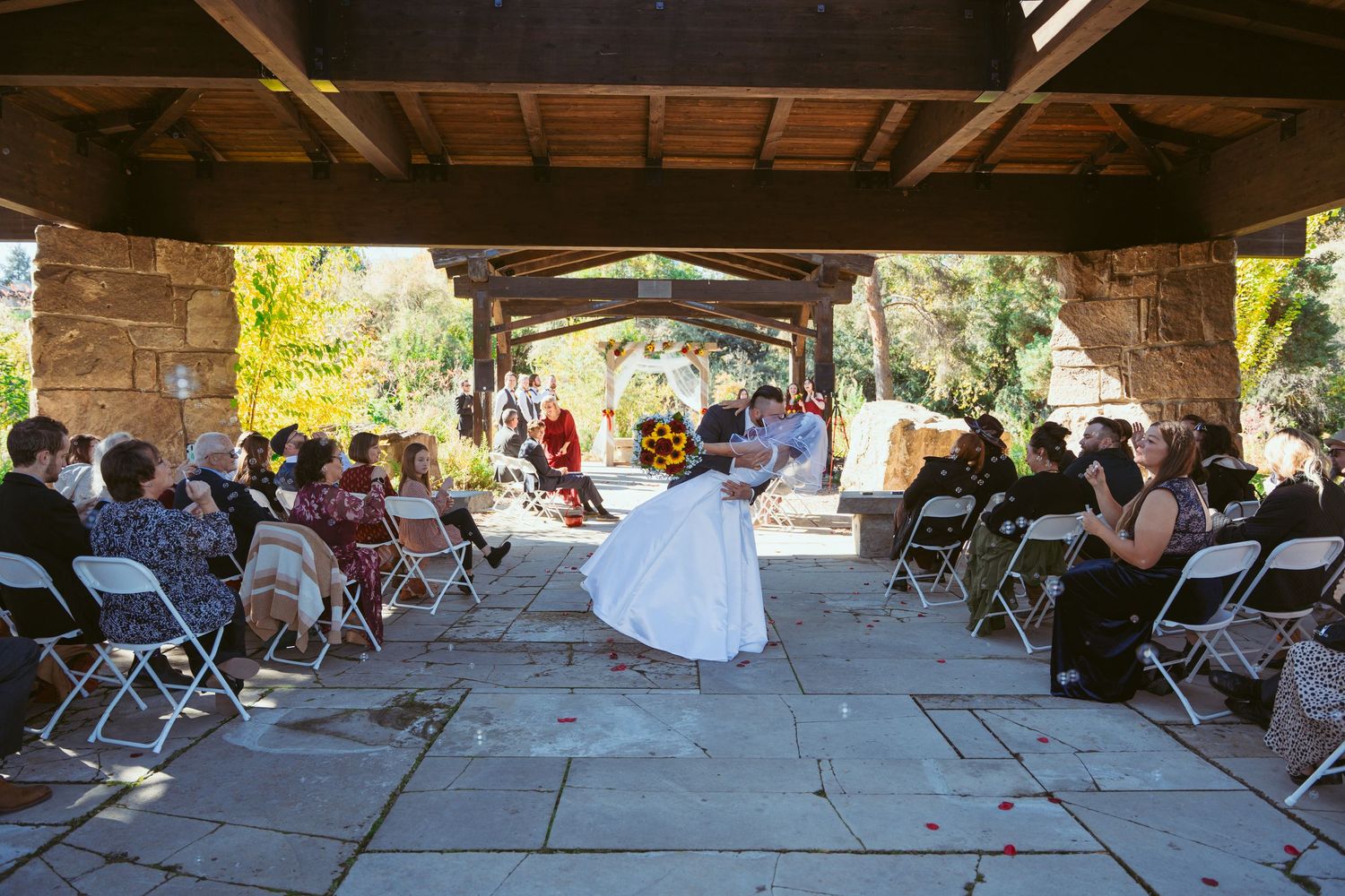 Rustic outdoor wedding venue with wooden beams and stone pillars in warm natural light.