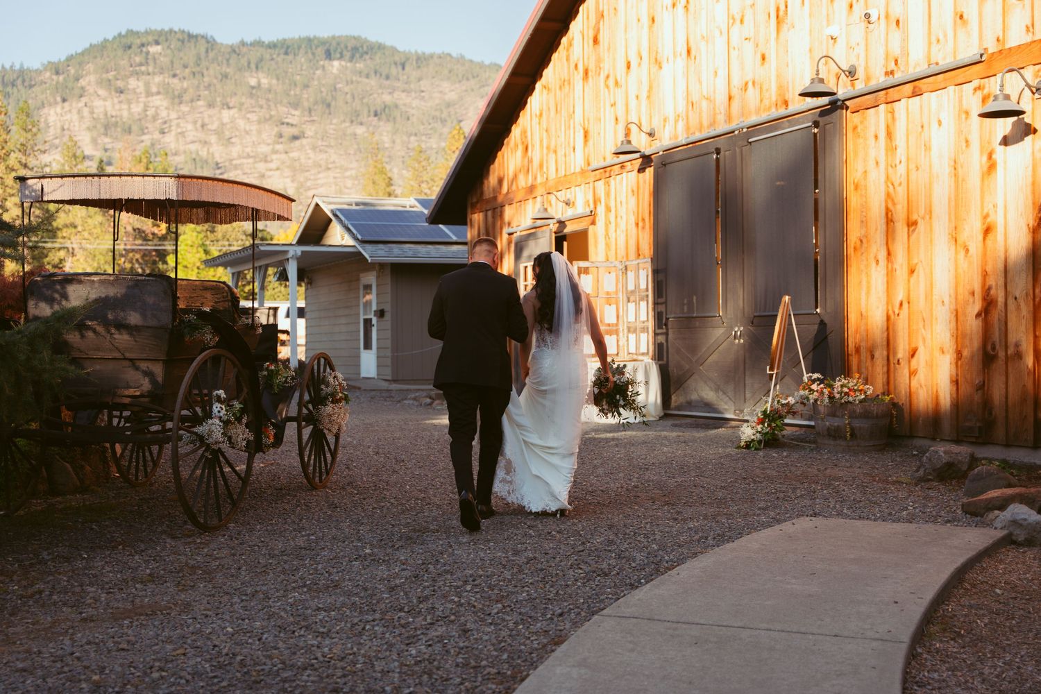 Rustic barn venue exterior with wedding party gathered outside at sunset.