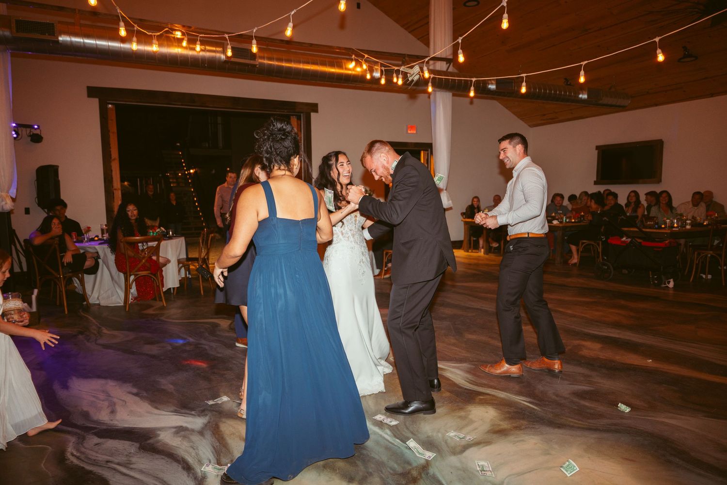 Wedding guests dancing and mingling under string lights at an indoor reception.