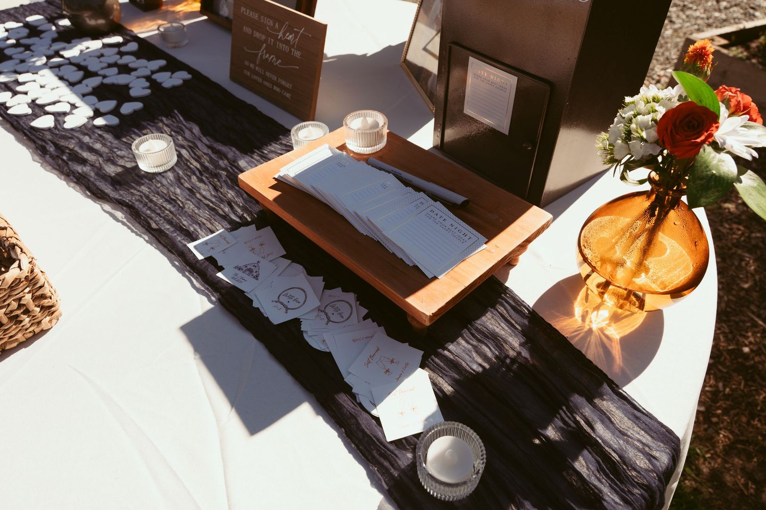 A wedding guest book display table with black linens and decorative elements in warm sunlight.