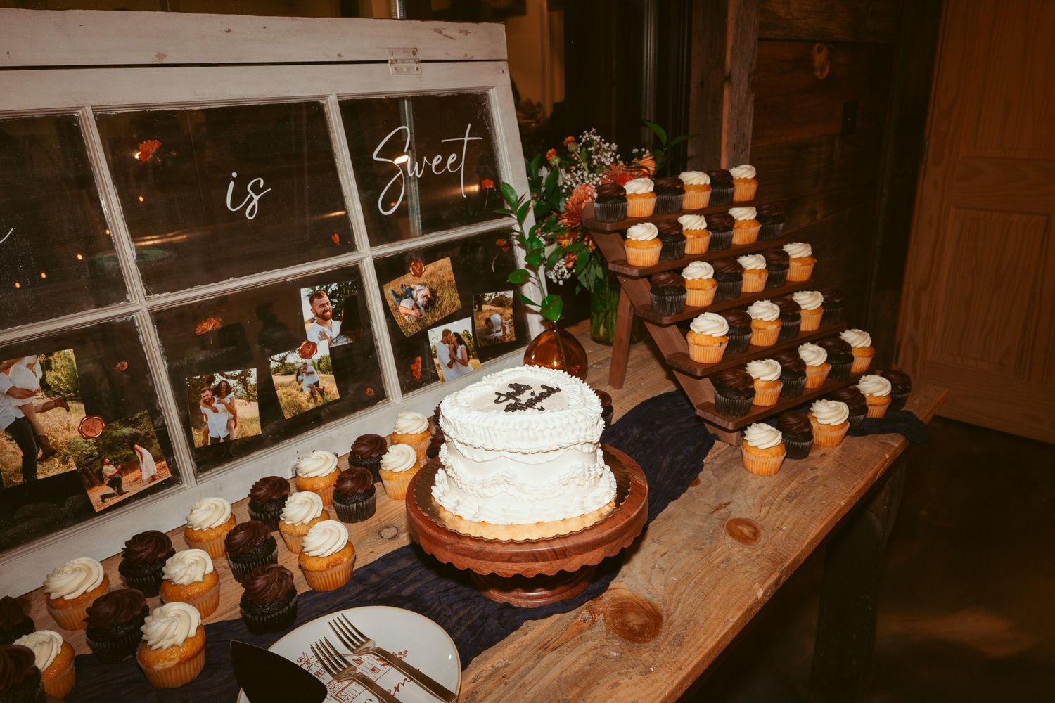 Wedding dessert table with white cake and cupcakes displayed with vintage window frame decor.