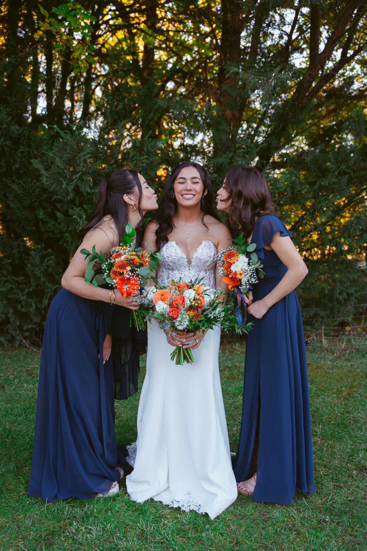 Wedding celebration group shares joyful moment outdoors with navy dresses and bright bouquets.
