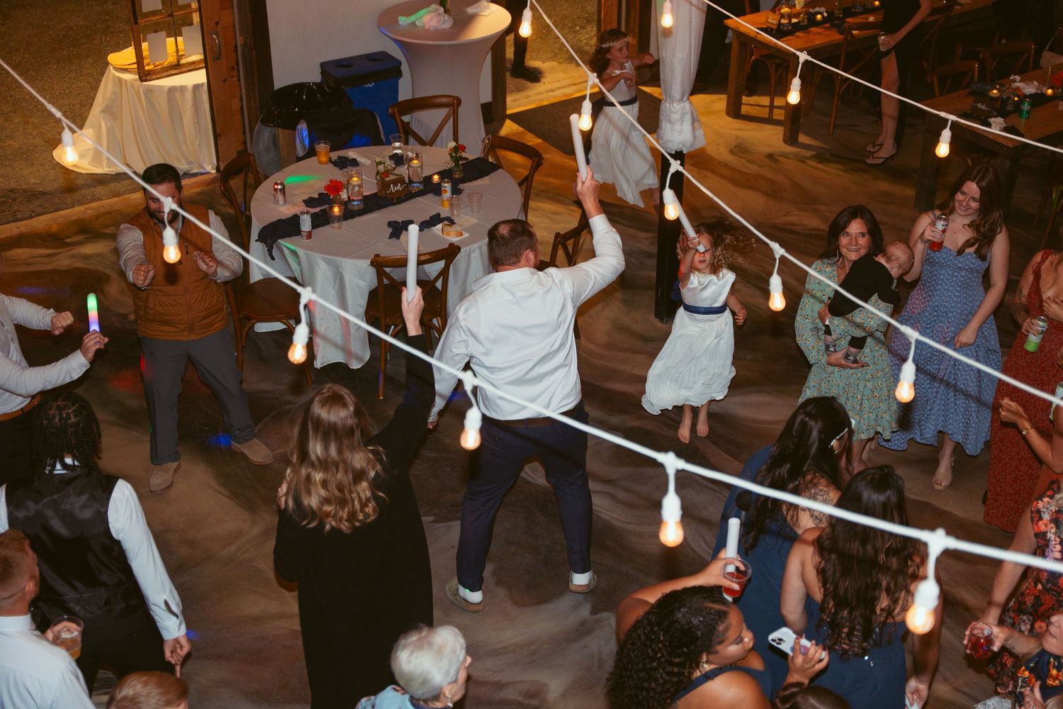 Lively dance floor with guests celebrating under hanging string lights at wedding reception.