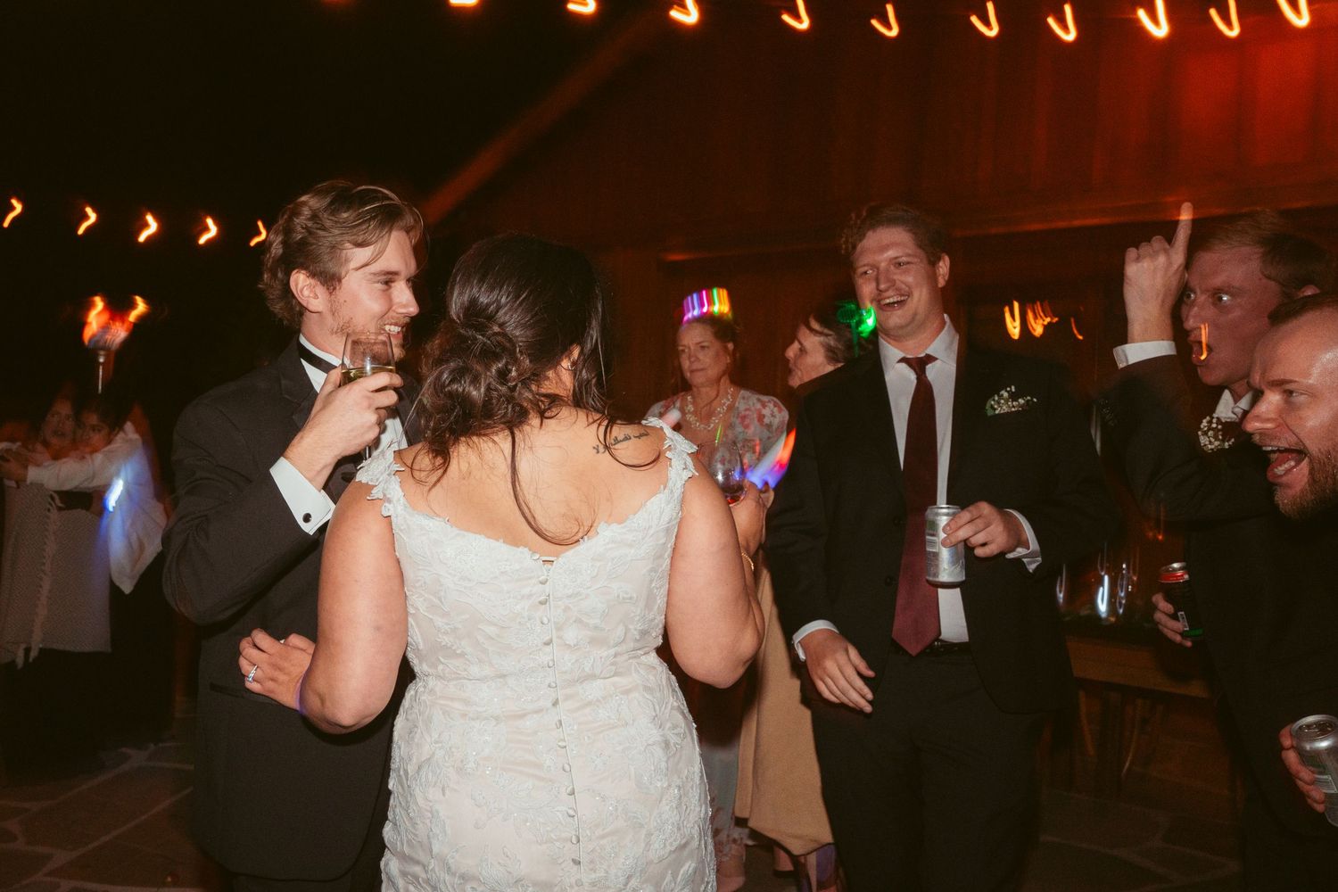 Wedding reception with guests dancing under rows of glowing string lights.