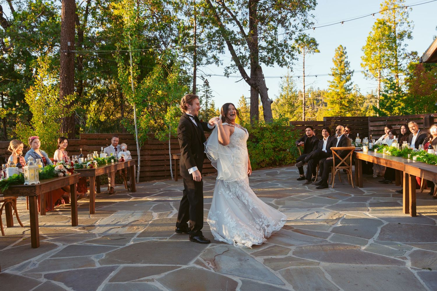 Wedding celebration on outdoor stone deck with couple dancing as guests watch from wooden benches.