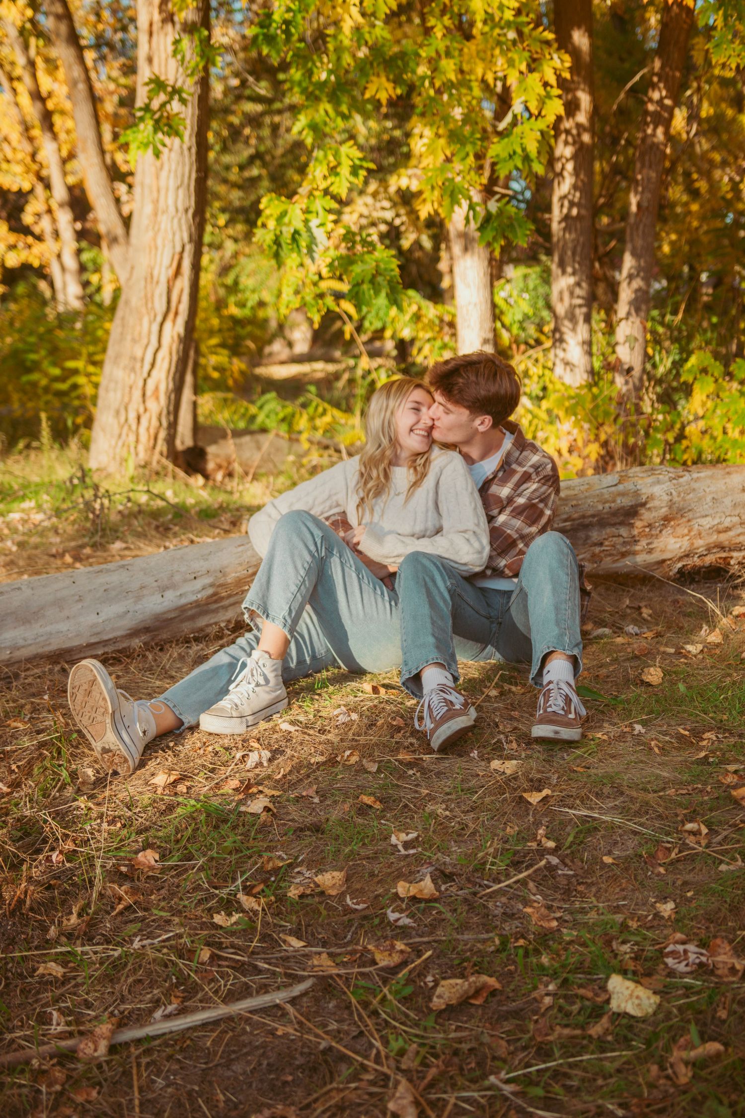 Couple lounges on forest floor surrounded by fall foliage and tree trunks.