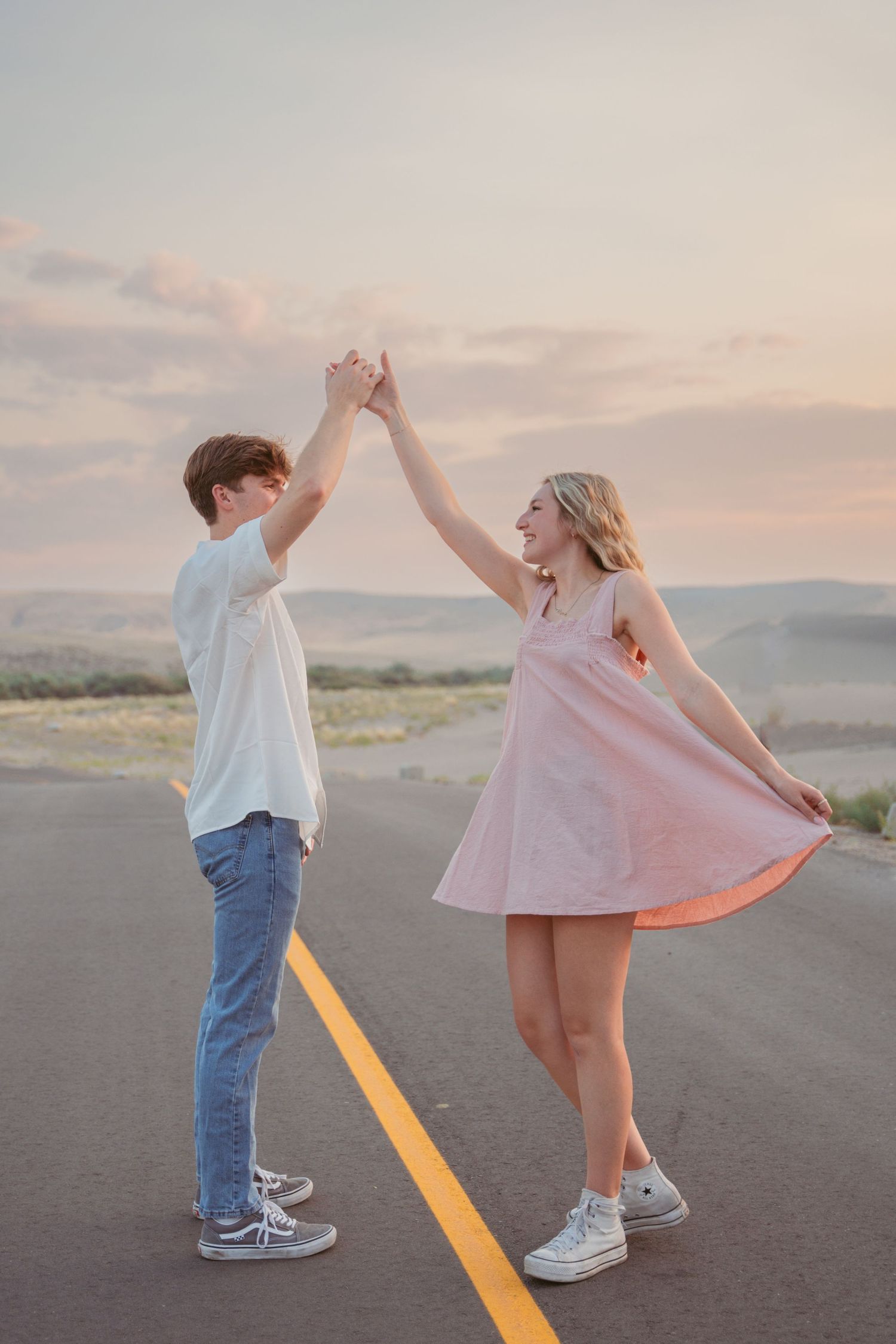 Playful couple dances together on an empty road at dusk with mountains in the distance.
