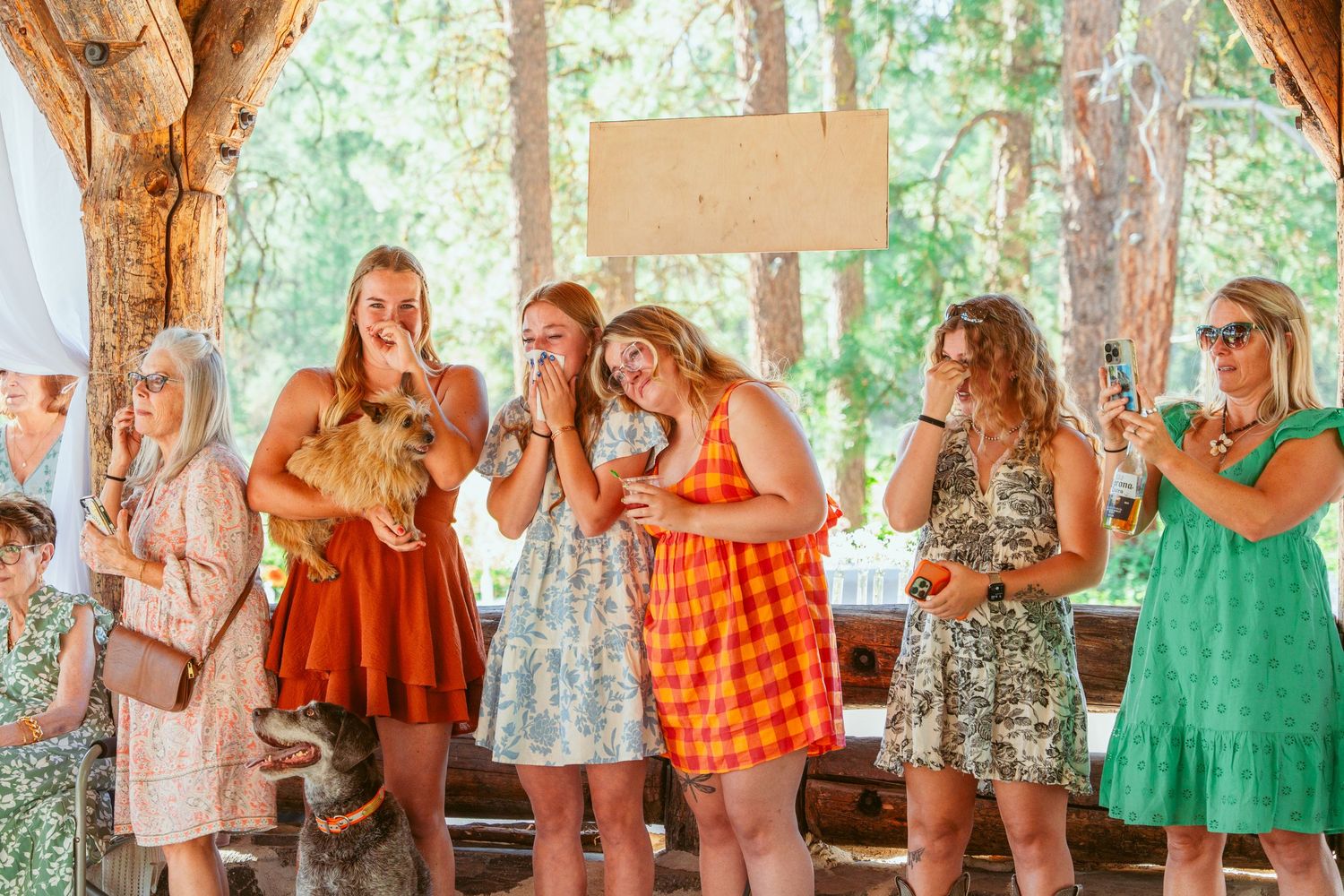 Summer wedding guests gathered in a rustic outdoor pavilion with wooden beams.
