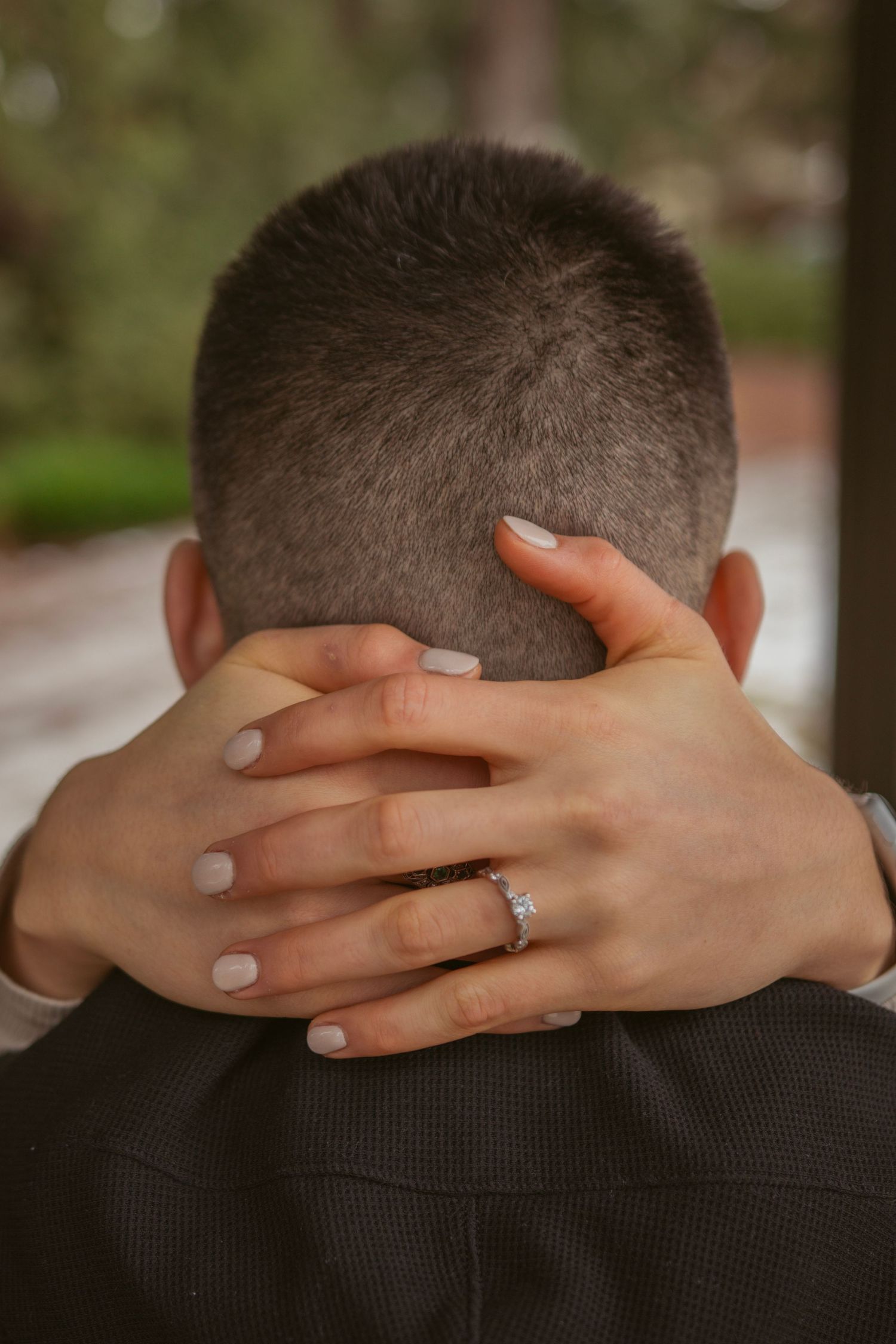 Close-up of hands gently placed on back showing engagement ring detail.