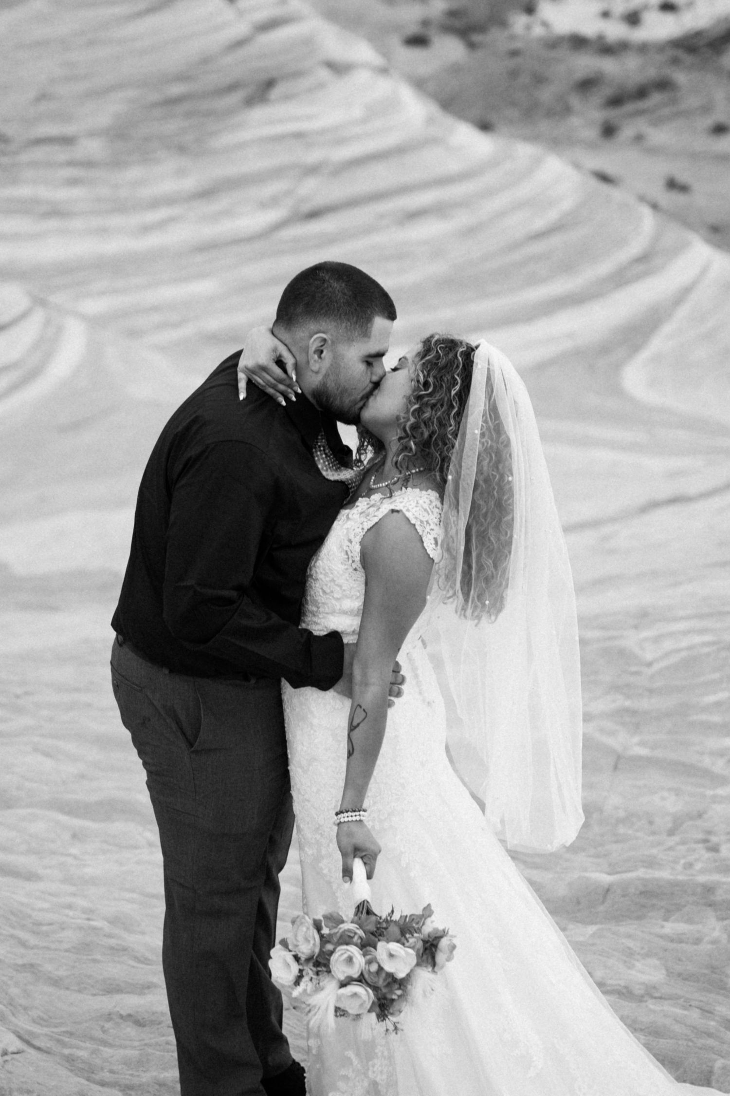 Black and white wedding photography capturing intimate moments on textured white sand dunes.