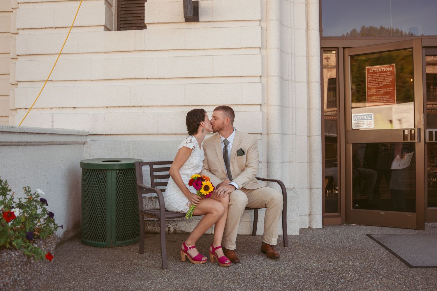 A couple sits together on concrete steps outside a white building.