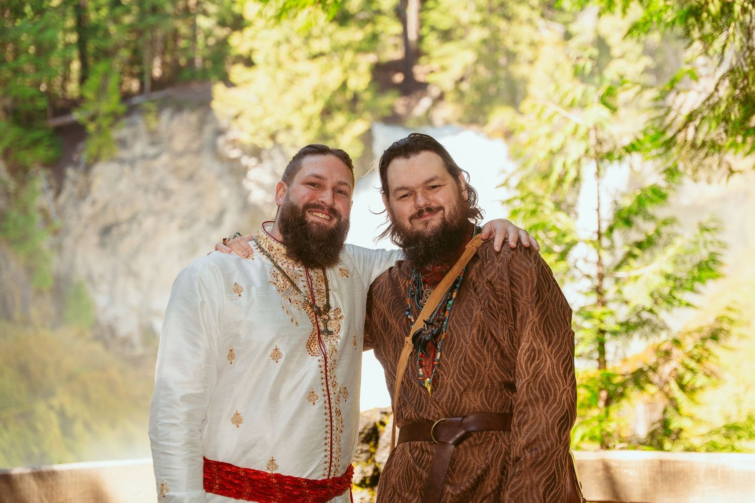 Two people in medieval wedding attire share a moment in a sunlit forest setting.