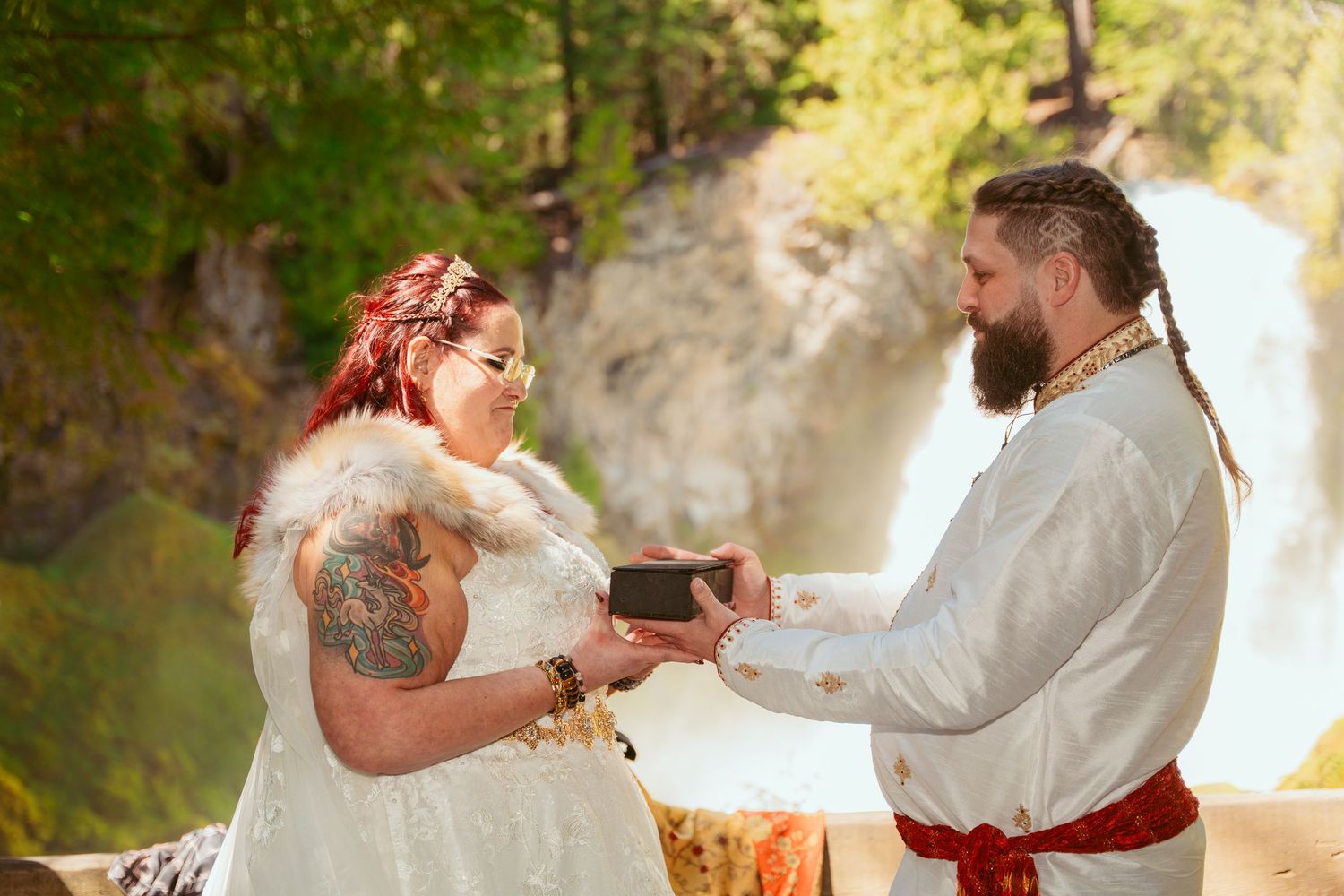 A couple in matching white outfits shares a romantic moment during their outdoor wedding ceremony.