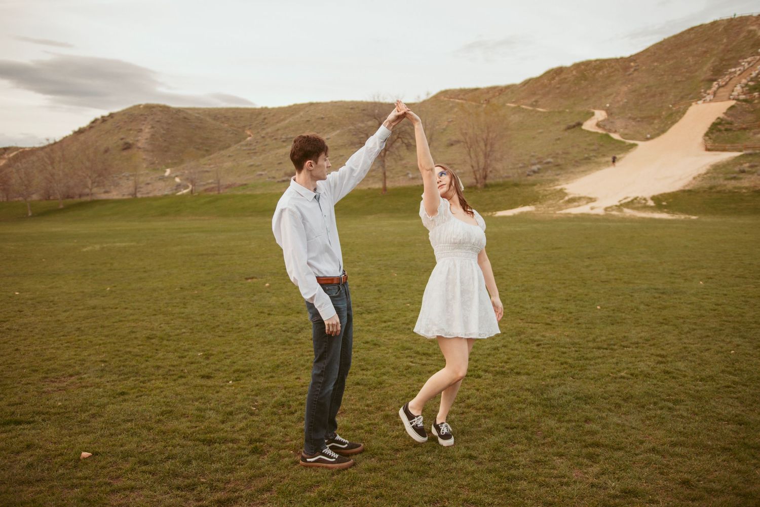 A couple dances playfully in a scenic mountain meadow during sunset.