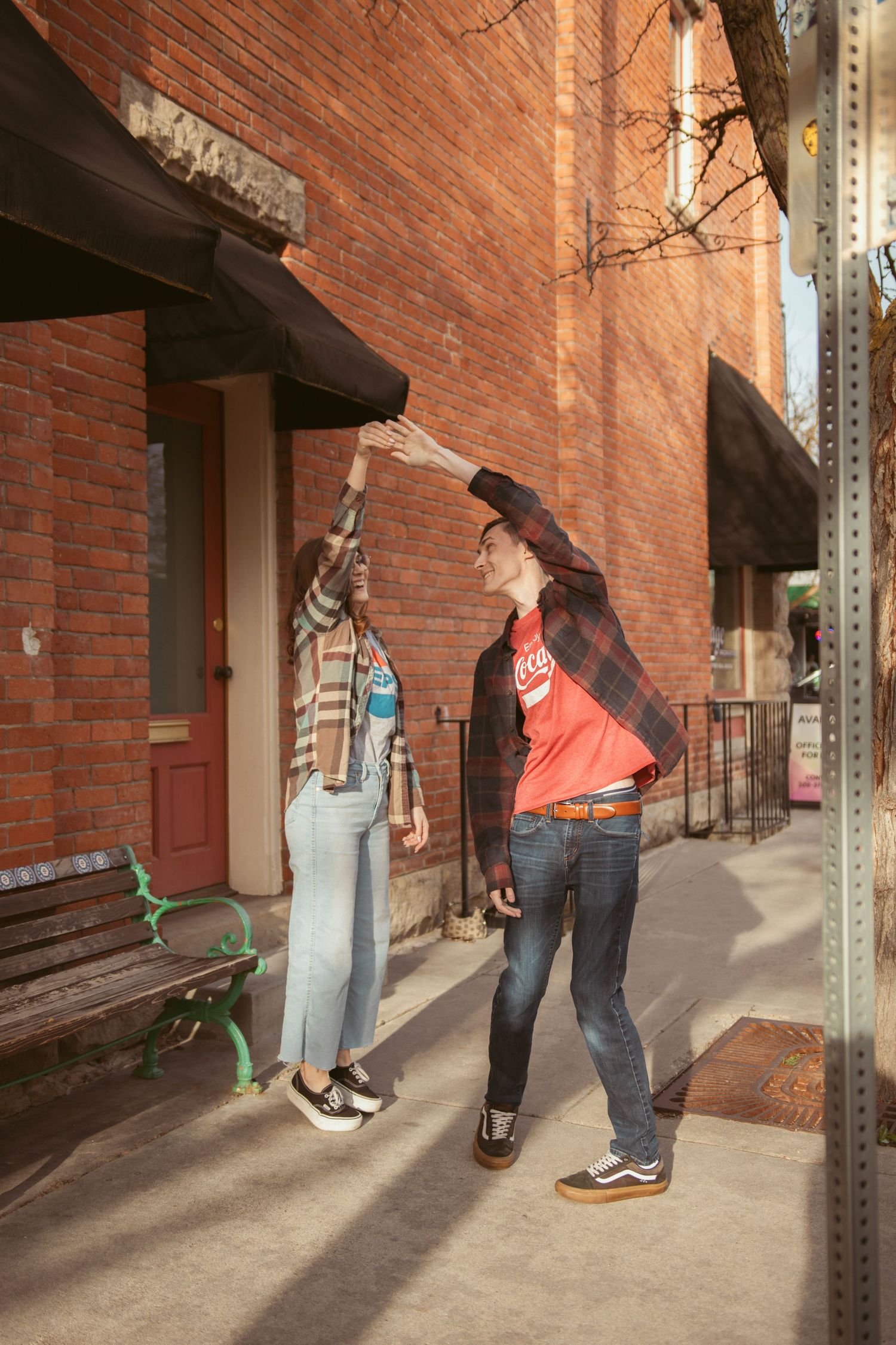Two people dance and pose dramatically on a sidewalk beside a historic brick building.