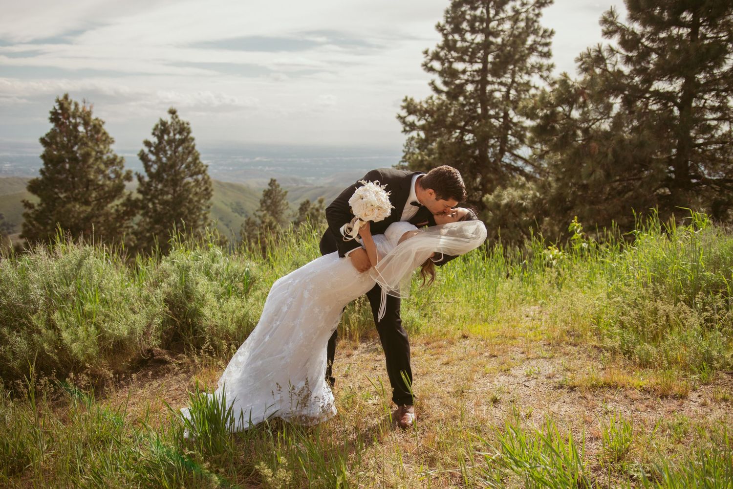 A romantic dip pose during a mountaintop wedding with pine trees in the background.