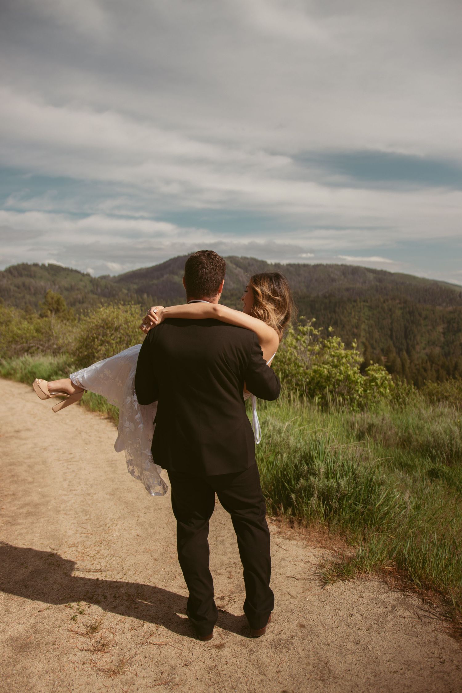 A tender embrace on a mountain trail with dramatic cloudy sky backdrop.