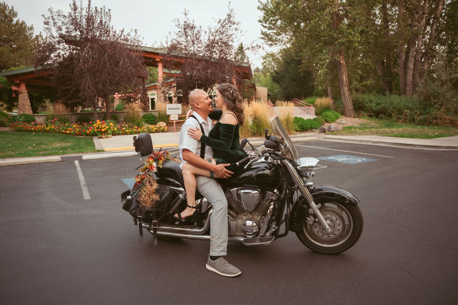 A couple poses with a motorcycle in a parking lot during sunset.