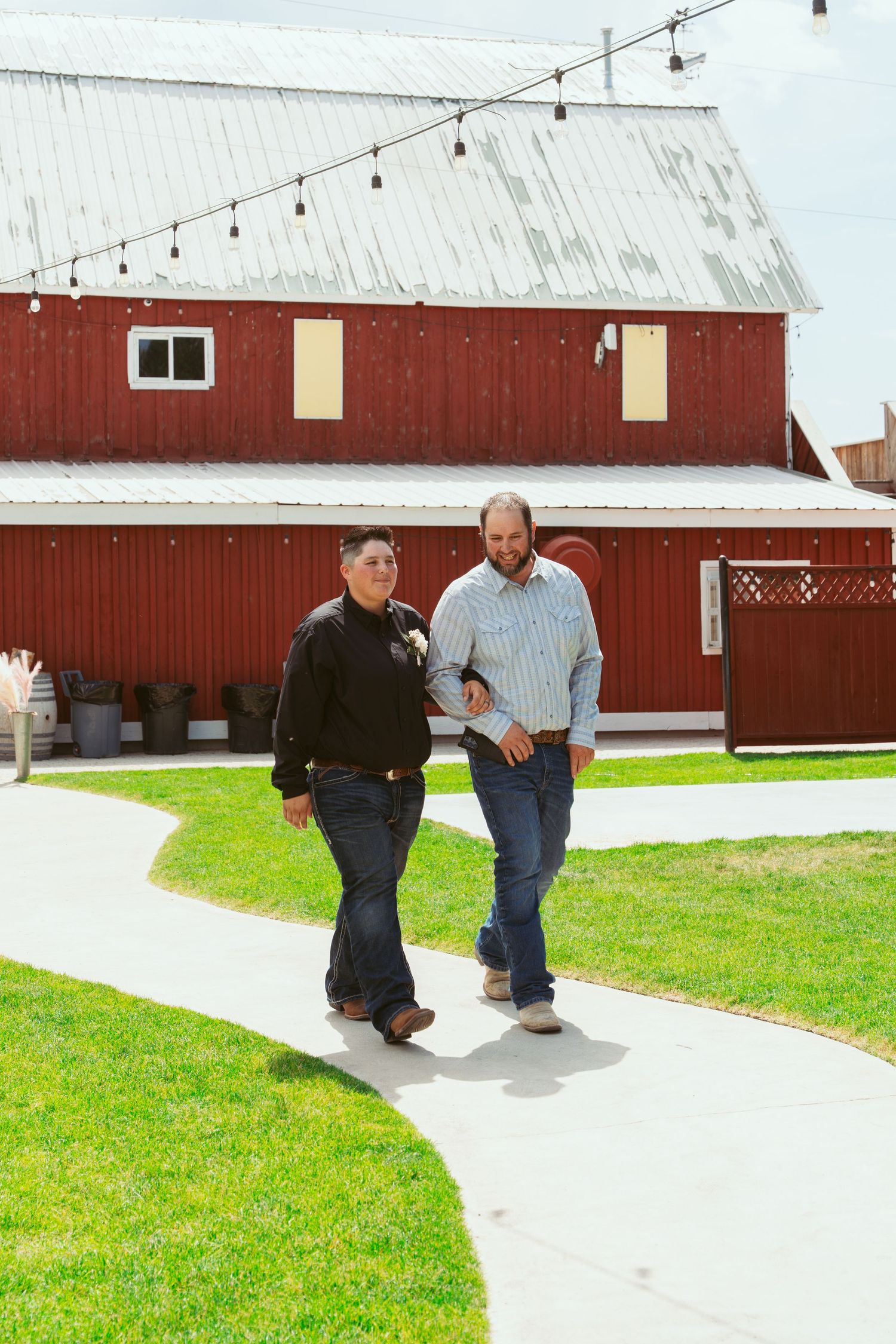 Red barn serves as backdrop for outdoor event with string lights and concrete pathway.