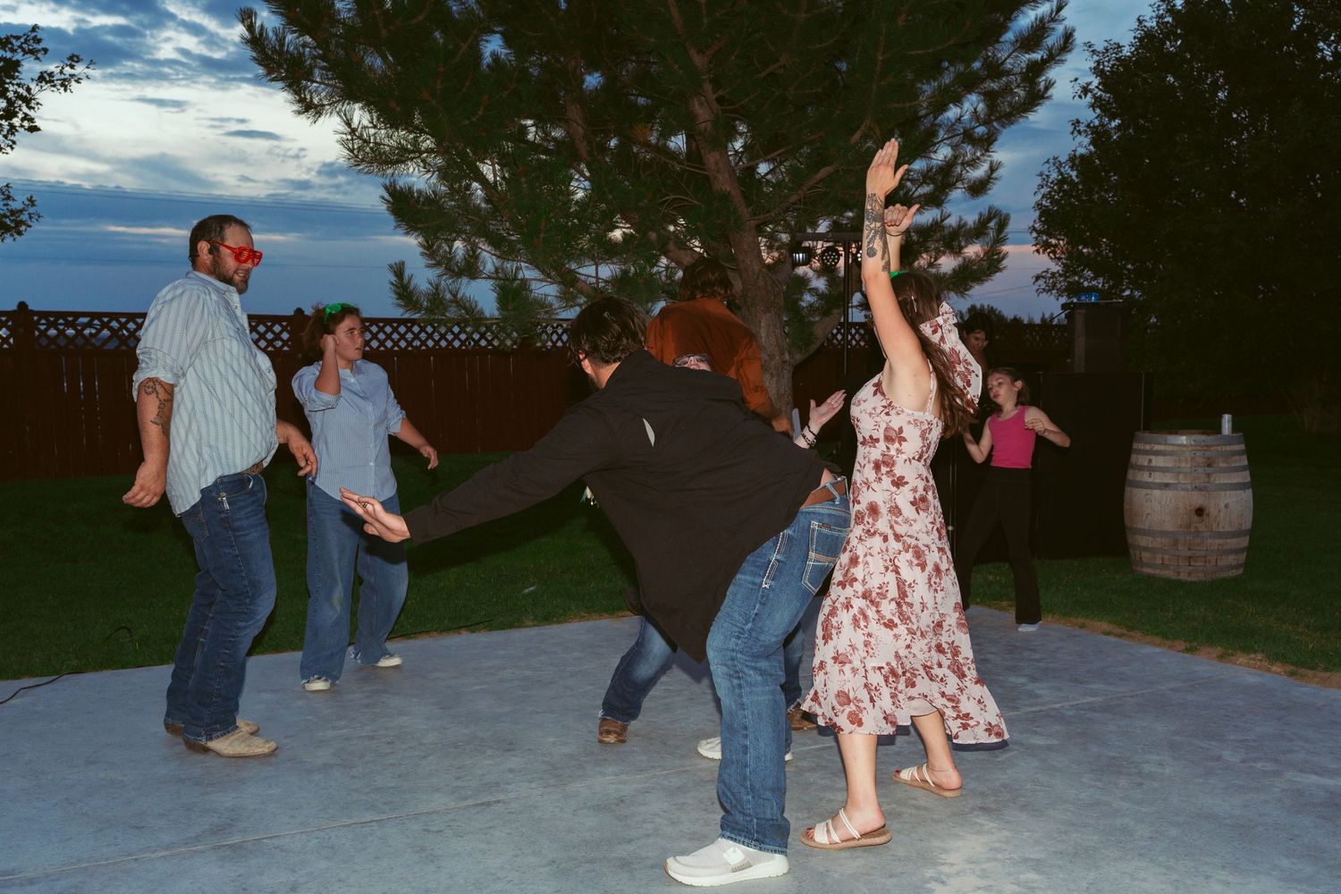 Couples dancing together at an outdoor evening event with trees in the background.