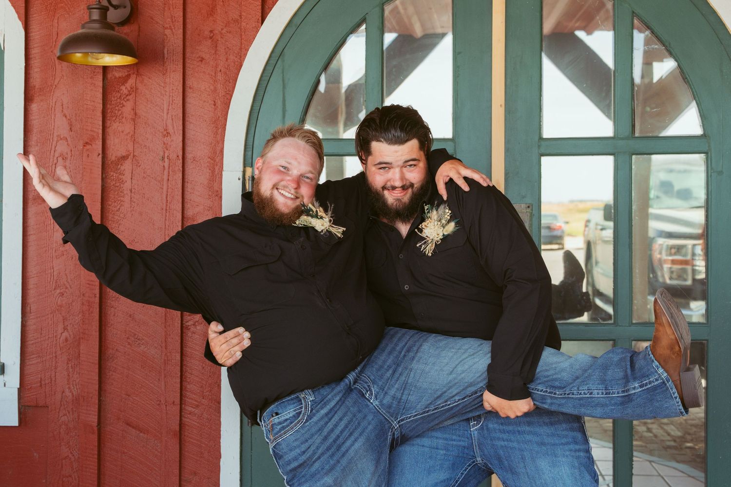 Wedding party poses playfully in front of red barn with teal arched doorways.