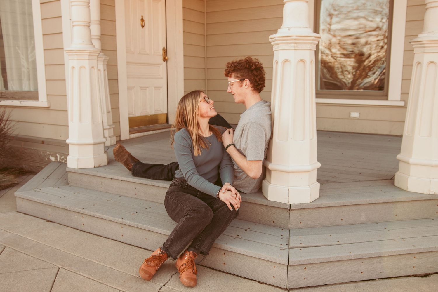 Couple in casual fall attire sharing romantic moments on a white porch with decorative columns.