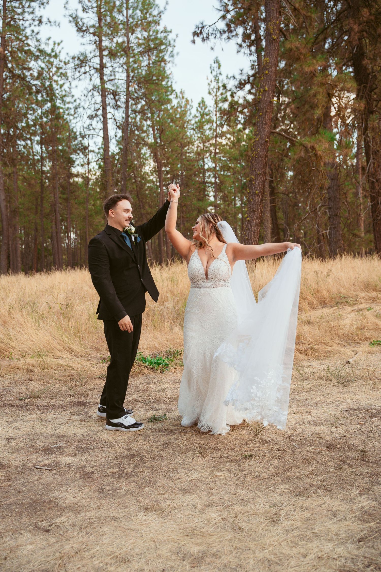 A couple dances and twirls playfully on a dirt path with pine trees in the background.