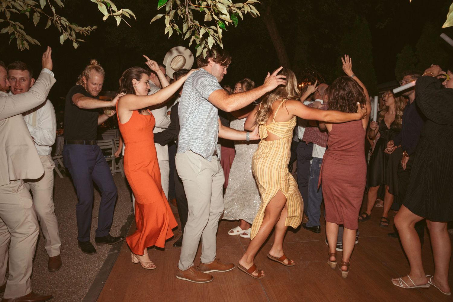 Large group of wedding guests performing a coordinated line dance on an outdoor dance floor.