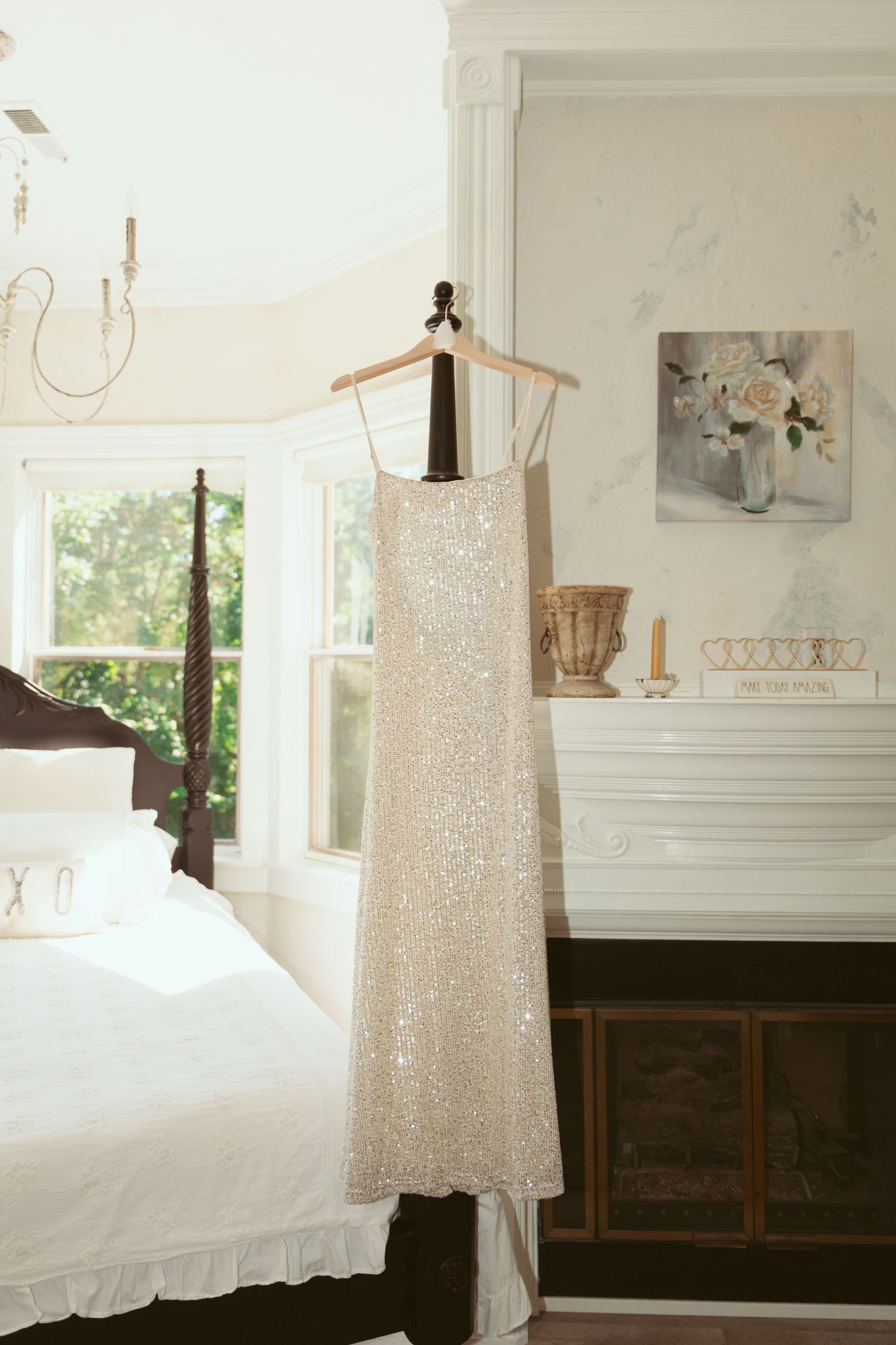 A sparkly white sequined dress hanging in a bright sunlit room with white walls and wooden furniture.