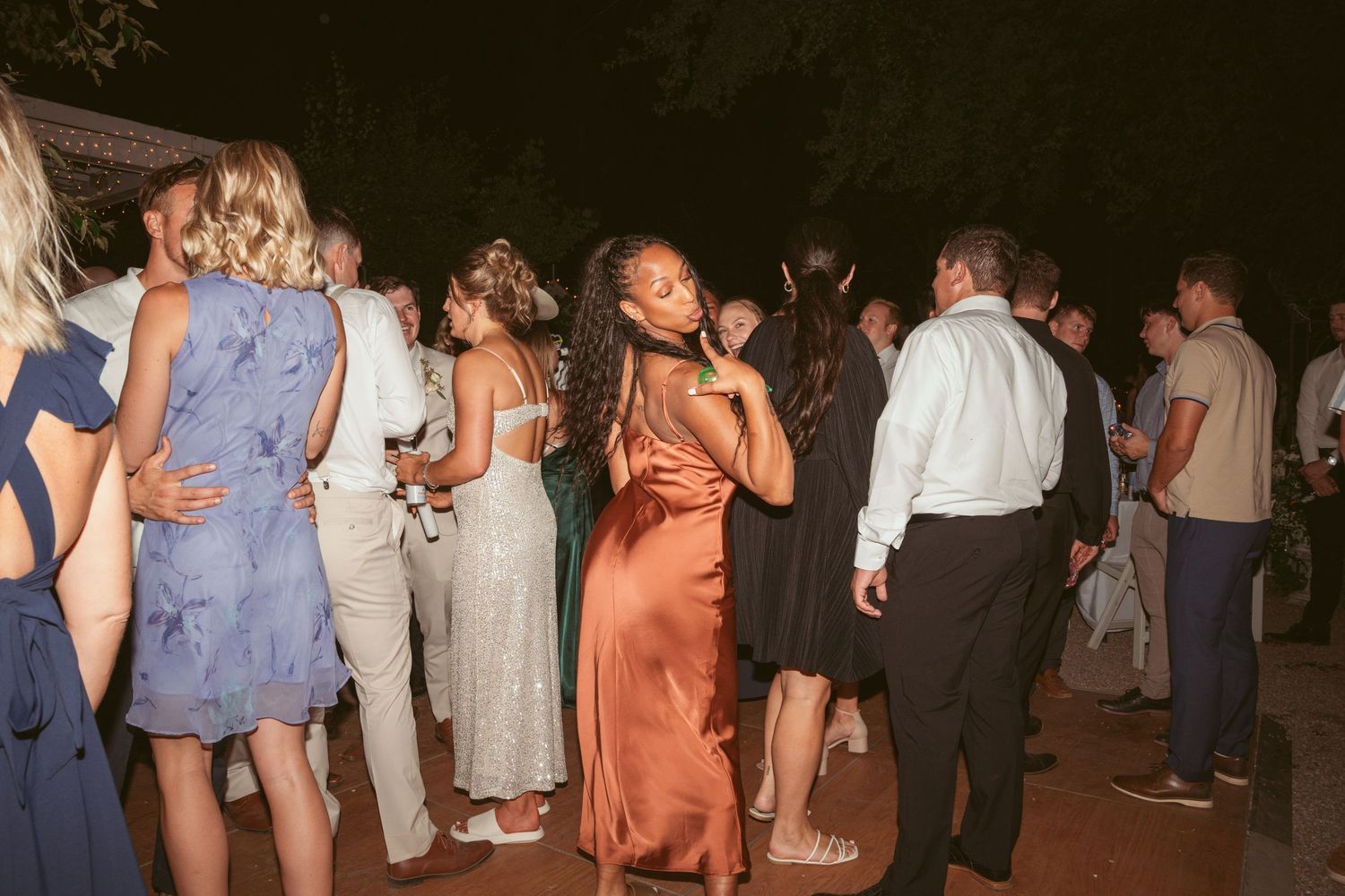 Party guests in formal dresses and suits mingling and dancing at an outdoor evening reception.