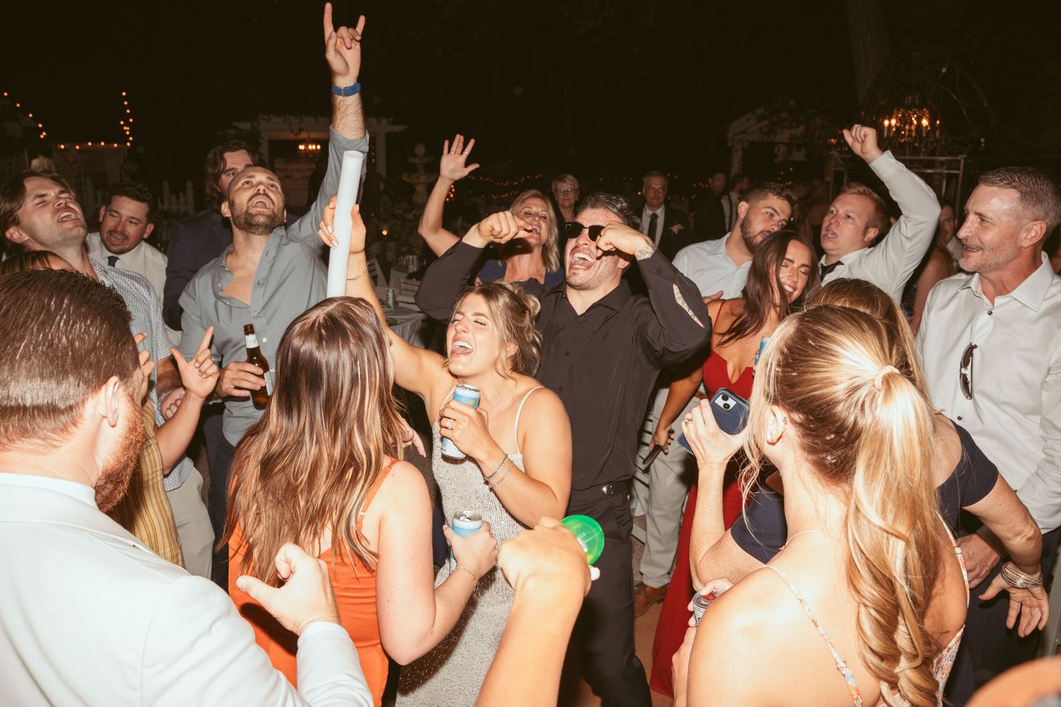 Lively crowd dances and celebrates at a wedding reception with hands in the air.