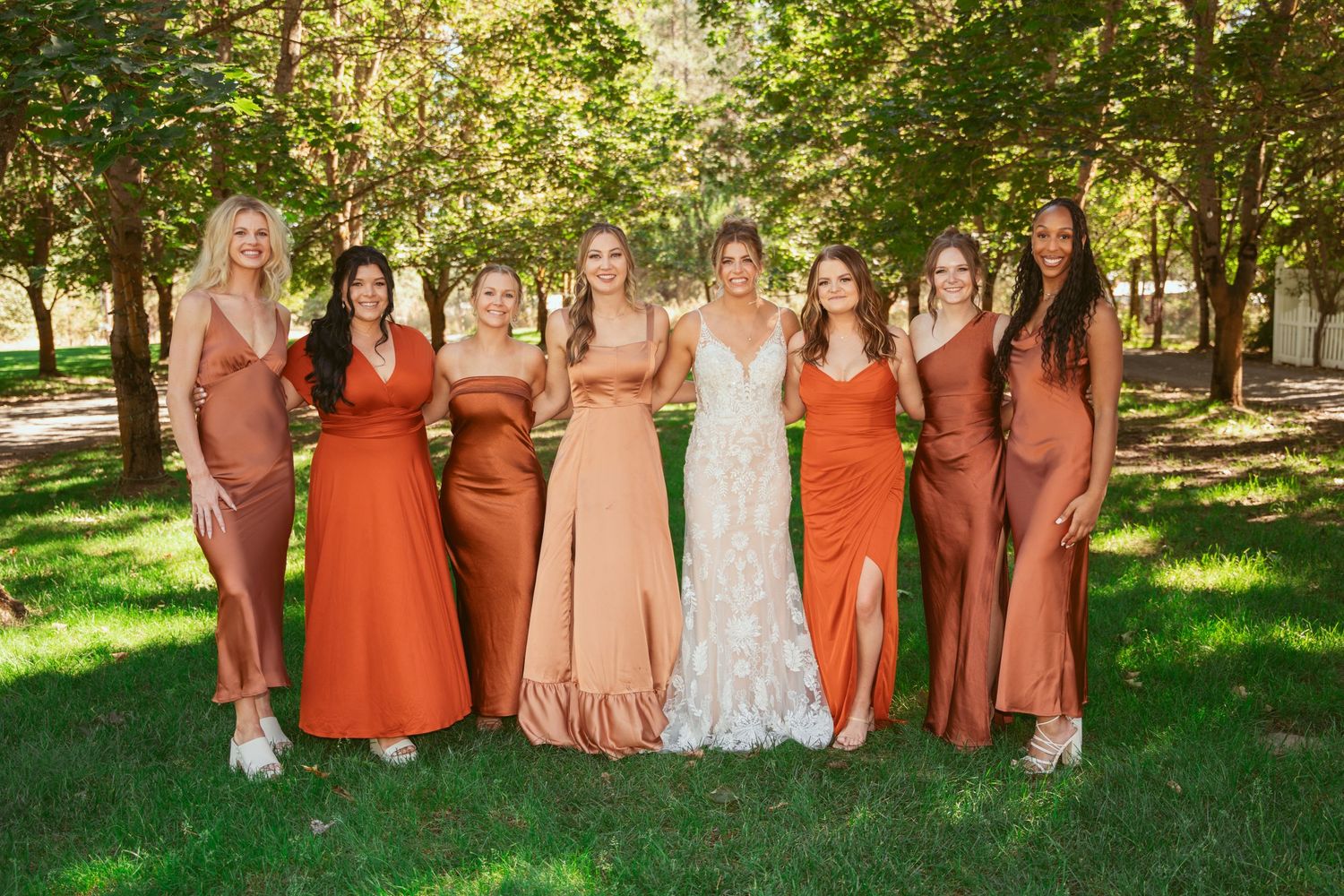 Bridal party wearing orange and blush dresses pose together in a scenic garden setting.