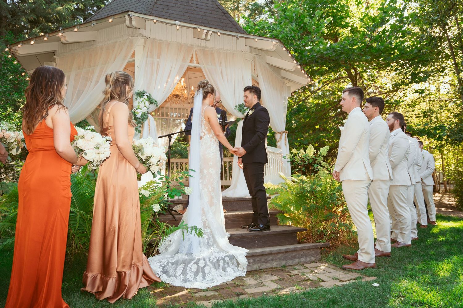 Wedding party photos being taken in garden with mix of coral dresses and white attire.