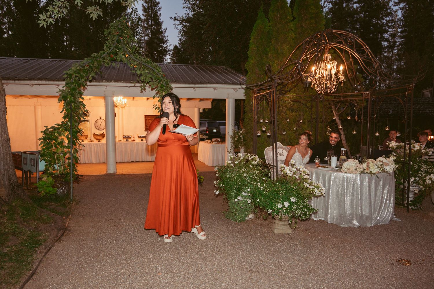 An outdoor wedding reception venue at dusk with elegant lighting and garden decorations.