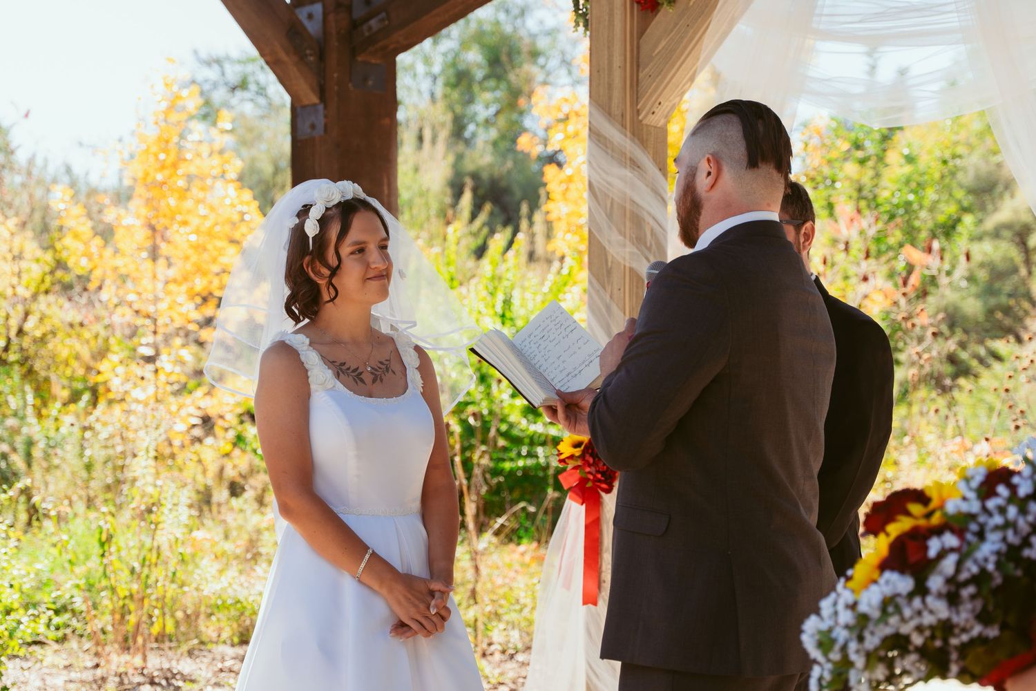 Outdoor autumn wedding ceremony with wooden beams and natural light filtering through.