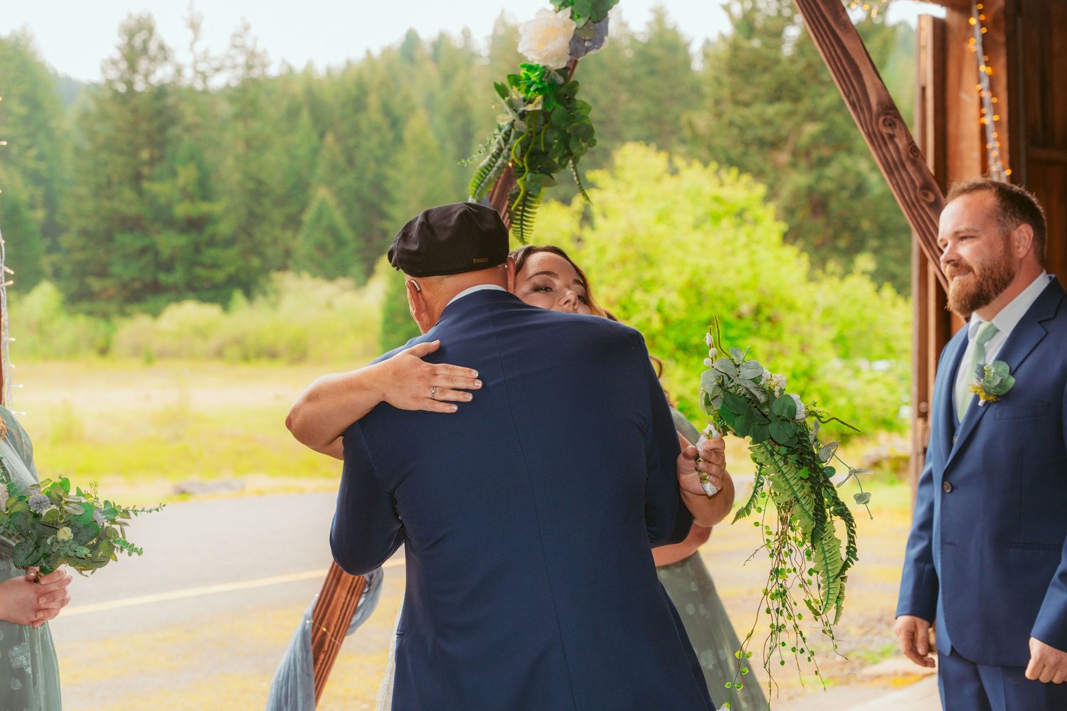 Couple sharing intimate first look moment in rustic wooden barn setting with forest backdrop.