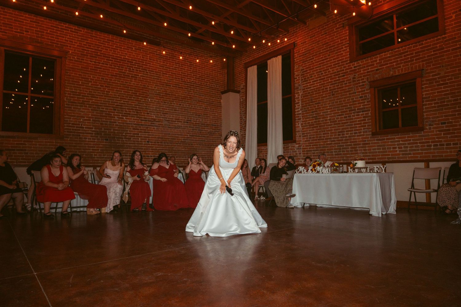 Wedding reception dance floor scene in a rustic brick venue with string lights.