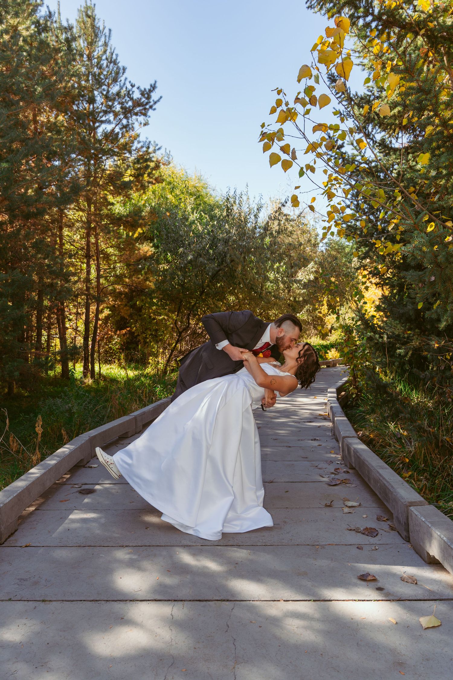 Romantic dip pose on wooden bridge with autumn scenery in background.