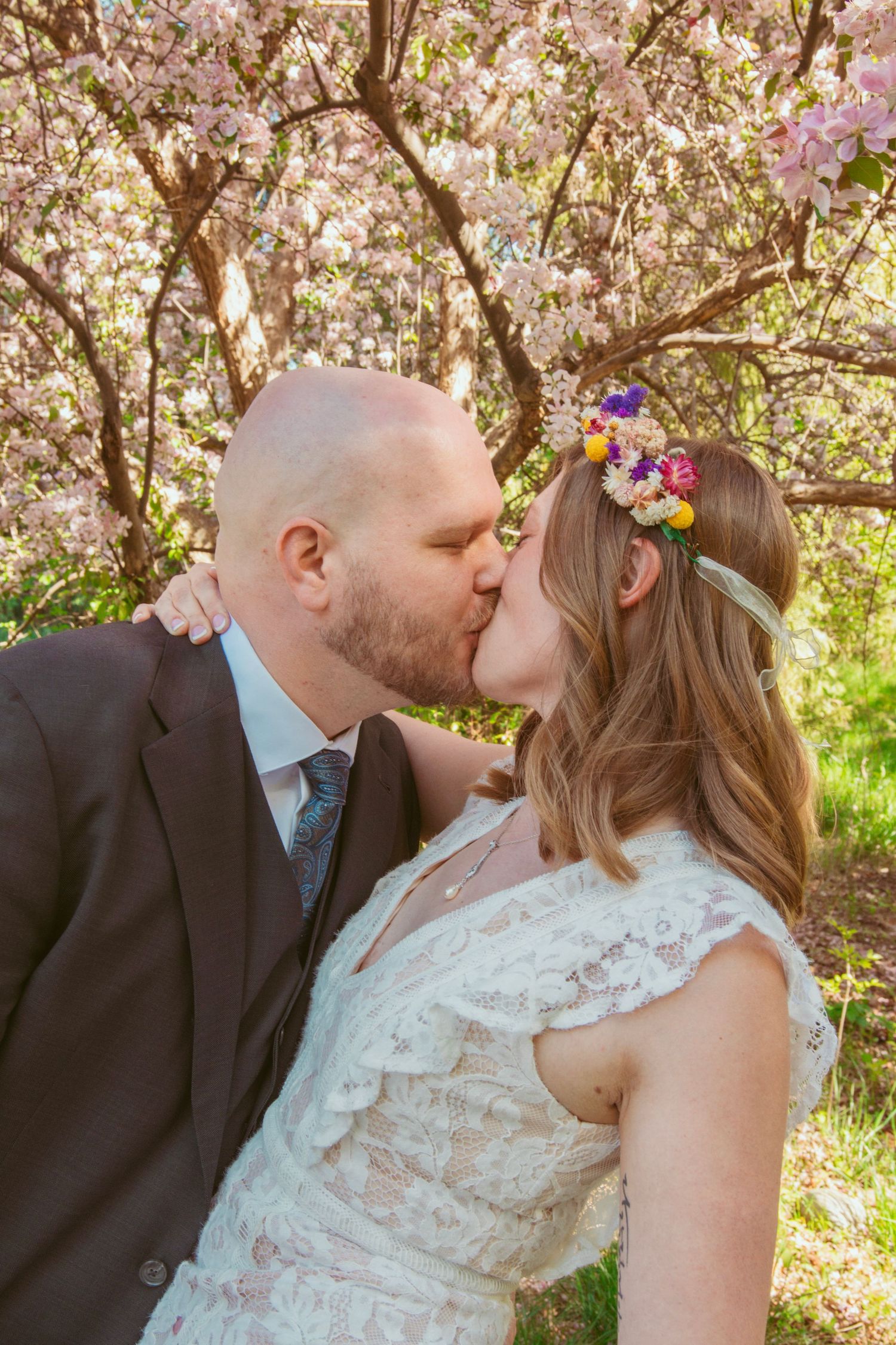 Couple shares intimate moments under blooming cherry trees with pink flowers.