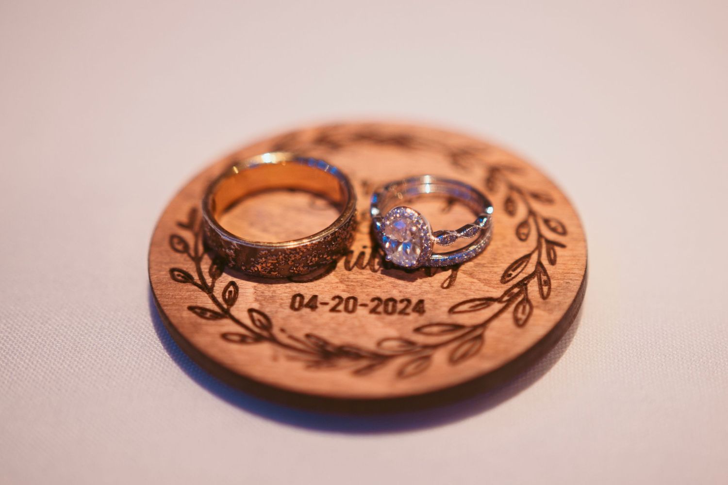 Wooden ring holder with engraved date and decorative leaf design.