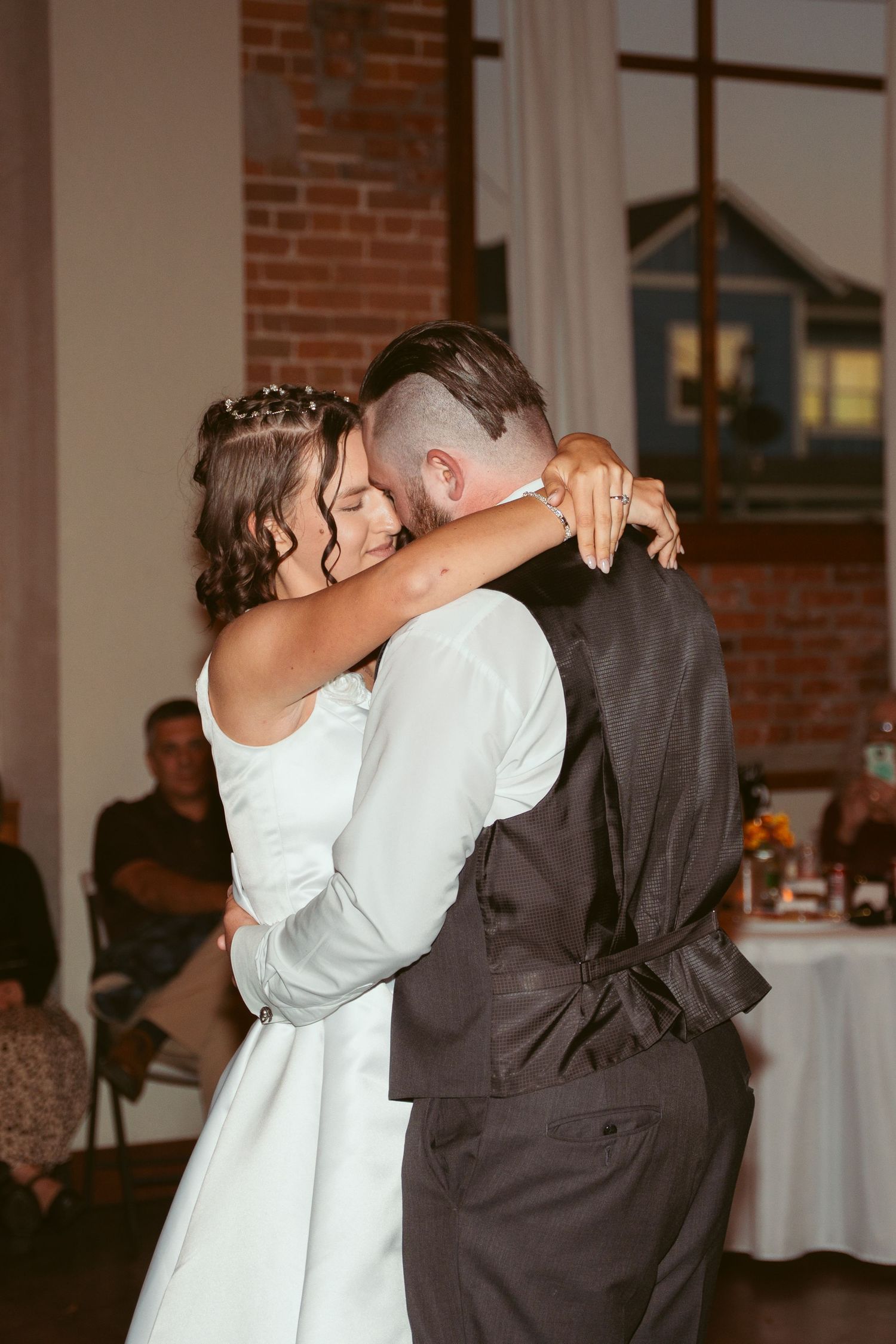 A couple shares a romantic dance move during their first dance at a rustic brick-walled wedding venue.
