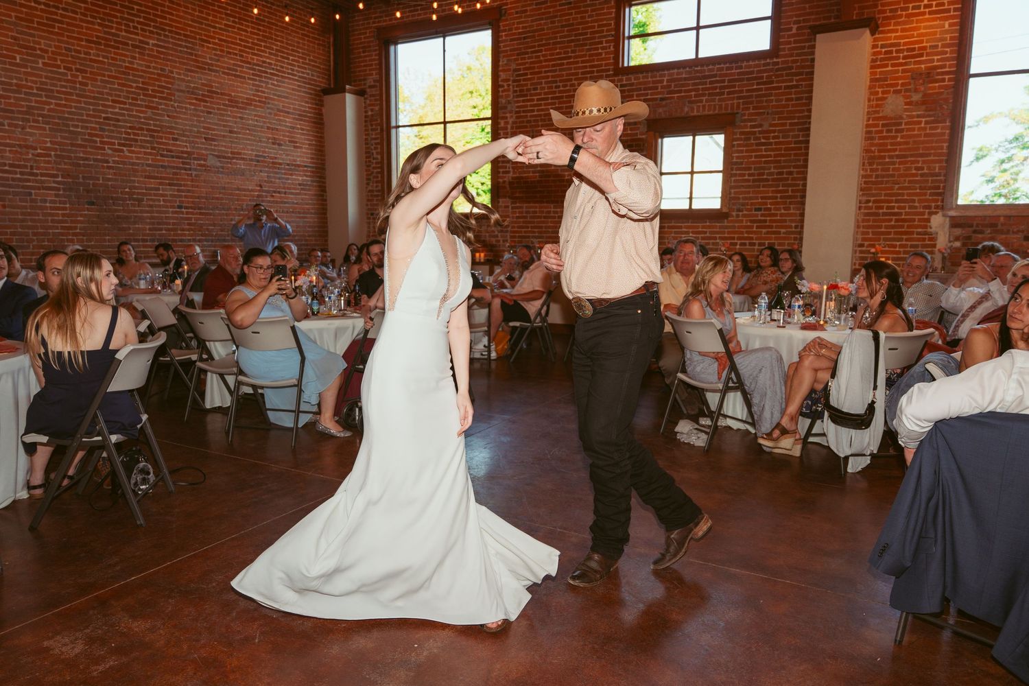 Wedding dance sequence captured in brick-walled venue with natural window lighting.