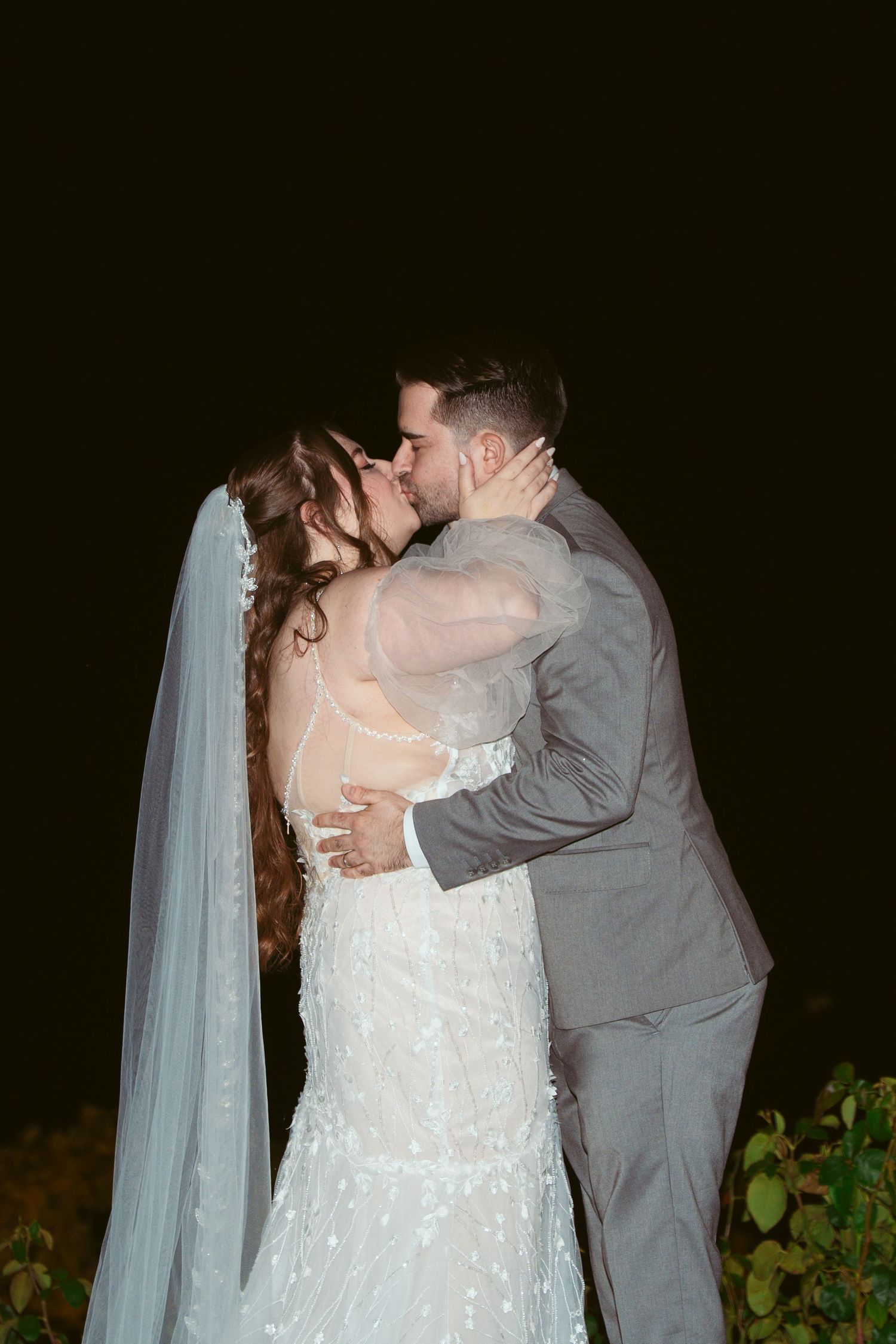 A romantic first kiss between newlyweds at an outdoor evening wedding ceremony.