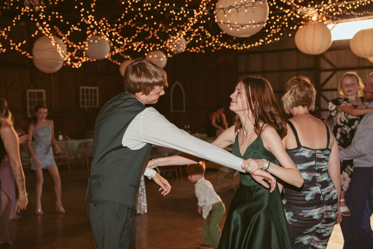 Guests performing choreographed dance moves at a rustic barn wedding reception.