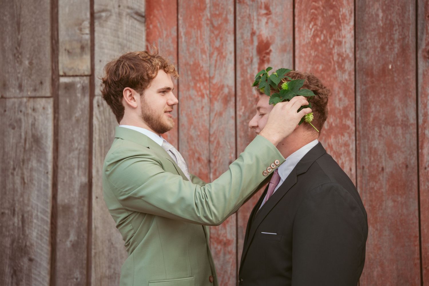 Wedding party members engage in playful pushing poses against rustic barn backdrop.