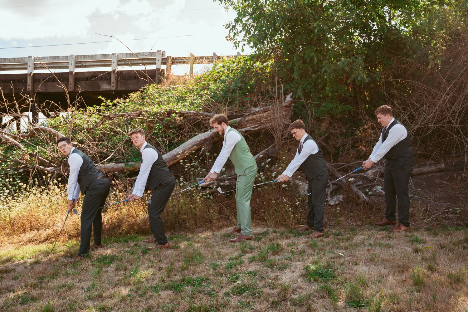 Groomsmen in sage green suits and vests pose playfully in sequence outdoors.