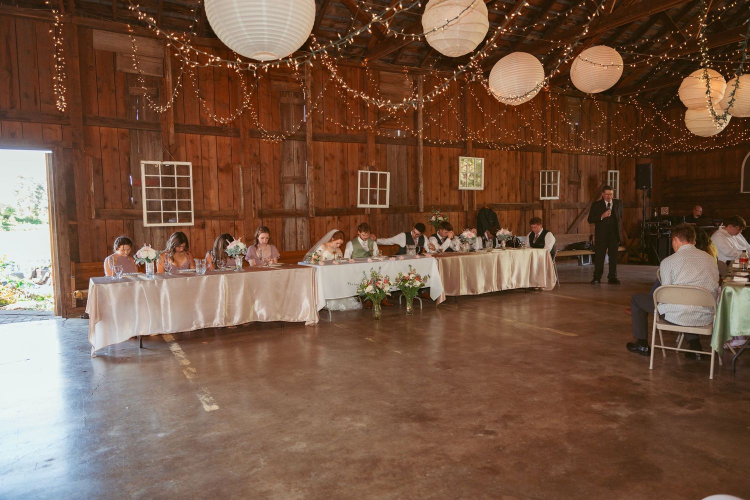 Panoramic view of a barn wedding venue with elegant table settings and hanging decorations.