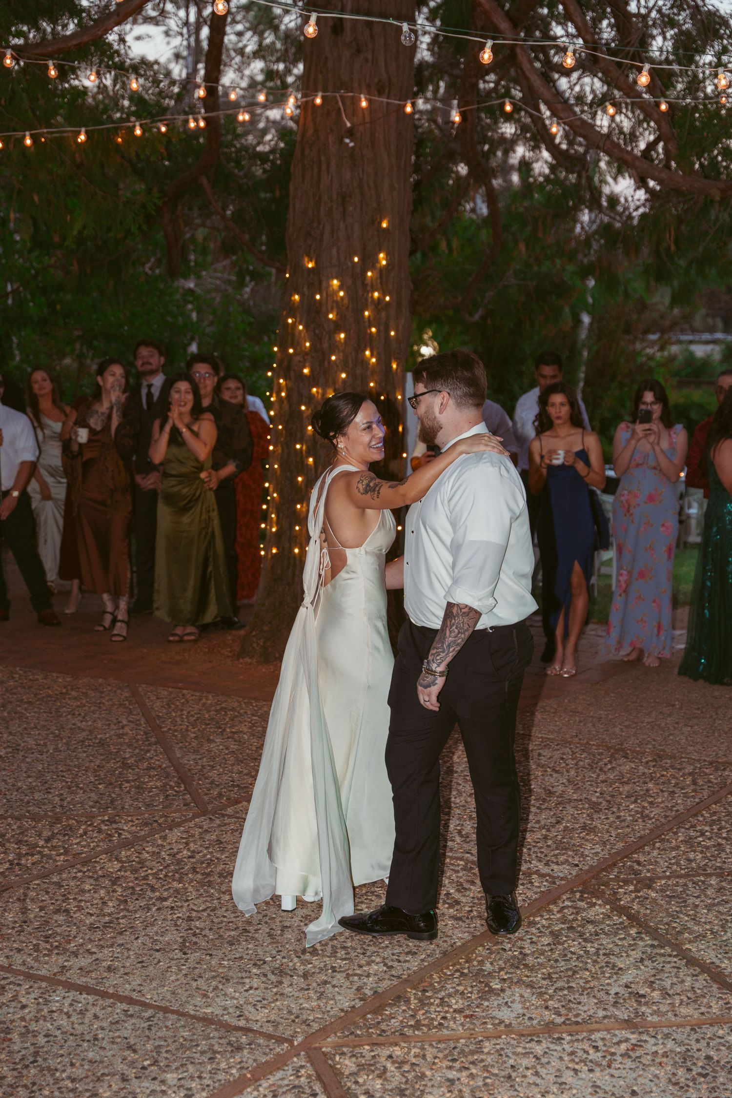 Couples dancing at twilight during an outdoor wedding reception with string lights overhead.