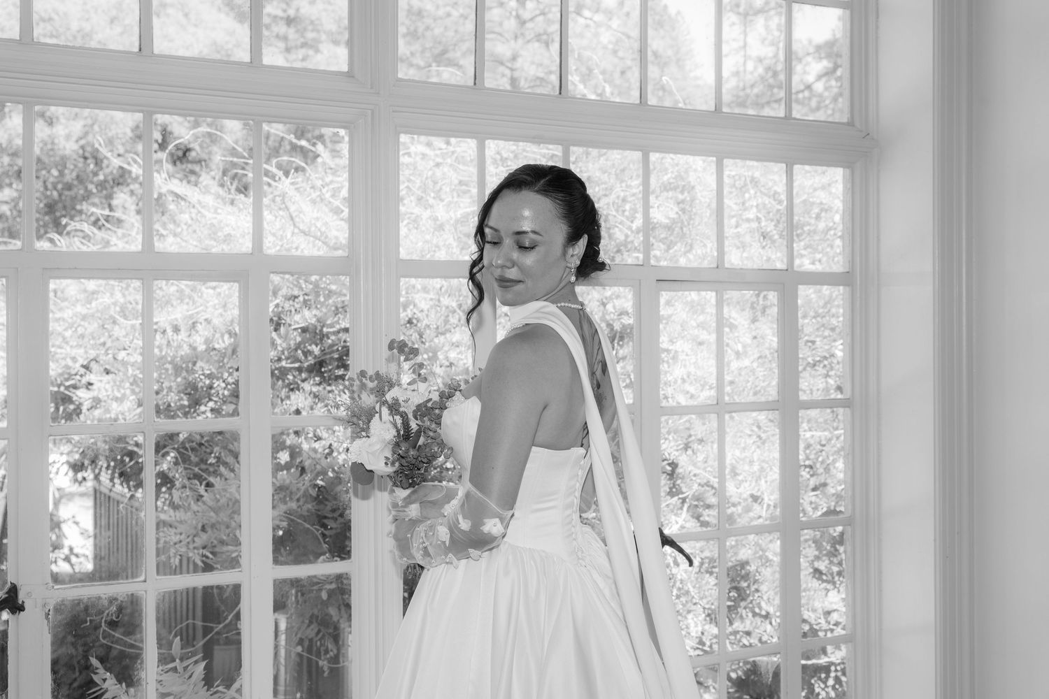 Bride preparing in a sunlit room with large windows and white decor.